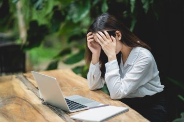 Asyalı iş kadını, stresli depresyon geçiriyor. Ahşap masada dizüstü bilgisayarla çalışıyor. Bunalımlı adam üzgün ciddi her yerden çalışıyor..