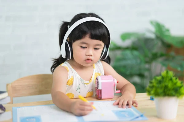 Cute little child wearing white headphone painting with colorful paints. Asian girl using wood color drawing color.Baby artist activity lifestyle concept.