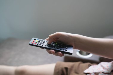 Close up Television remote control in young woman pink shirt hands pointing to tv set and turning it on or off. select channel watching tv on sofa at home in the living room relax.