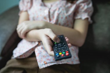 Close up Television remote control in young woman pink shirt hands pointing to tv set and turning it on or off. select channel watching tv on sofa at home in the living room relax.