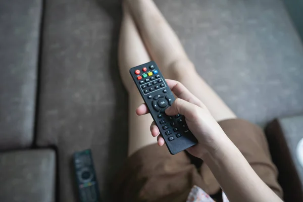 Close up Television remote control in young woman pink shirt hands pointing to tv set and turning it on or off. select channel watching tv on sofa at home in the living room relax.