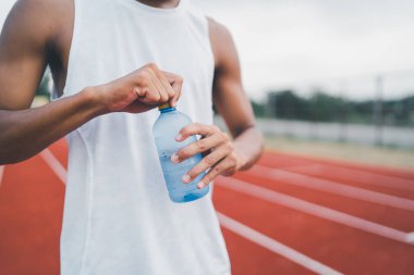 Close up of hand sport man hold bottle water runner tired and thirsty after running workout drinking water. Sport man concept