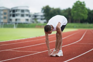 Athletes sport man runner wearing white sportswear to stretching and warm up before practicing on a running track at a stadium. Runner sport concept.