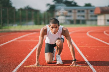 El koşucusu sabah stadyumdaki kulvarda atlet antrenmanına hazır. Koşmak için beyaz yelek giyen koşucu yarışa hazırlanıyor..