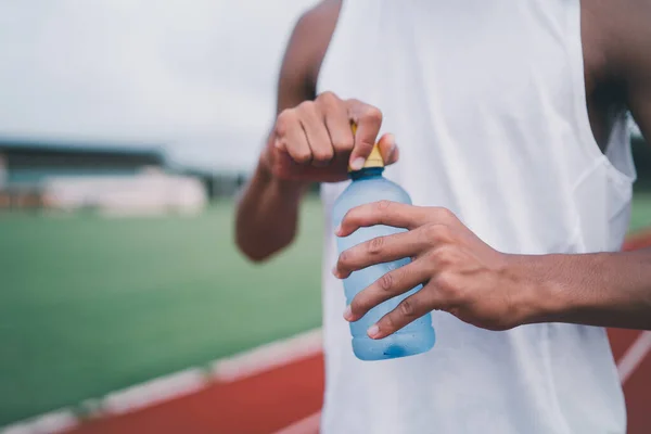 Close up of hand sport man hold bottle water runner tired and thirsty after running workout drinking water. Sport man concept