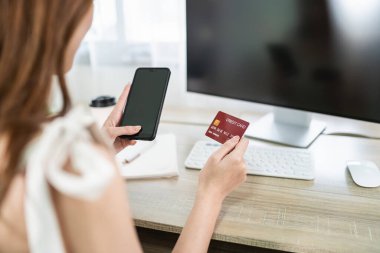 Woman holding credit card and using mobile to shopping online. asian woman working at home. Online shopping, e-commerce, internet banking, spending money, working from home concept.