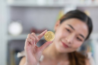 Asian woman girl smiling holding gold bitcoin crypto currency blockchain on wood table desk in living room at home. Crypto currency blockchain Saving investment wealth concept.
