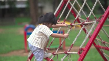 Cute asian girl smile play on school or kindergarten yard or playground. Healthy summer activity for children. Little asian girl climbing outdoors at playground. Child playing on outdoor playground.
