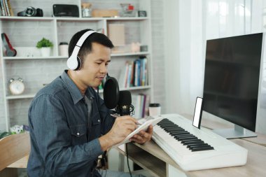 Asian man wearing white headphones compose song and learning online or record sound with a microphone and use computer recording music program. sound engineer man record music.
