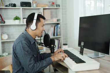 Asian man wearing white headphones sing a song learning online or record sound with a microphone and use computer recording music program. sound engineer man record music.