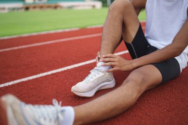 Athletes sport man runner wearing white sportswear sitting ankle sprain feeling pain his ankle or leg or knee after practicing on running track at stadium, copy space. Runner sport injury concept.