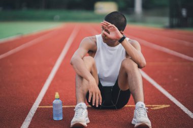 Athletes runner sport man resting bottle water tired and thirsty  practicing on a running track at a stadium. Running workout drinking water. Sport man run concept.