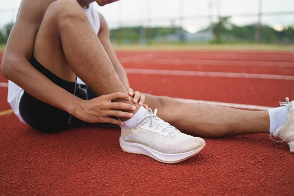 Athletes sport man runner wearing white sportswear sitting ankle sprain feeling pain his ankle or leg or knee after practicing on running track at stadium, copy space. Runner sport injury concept.