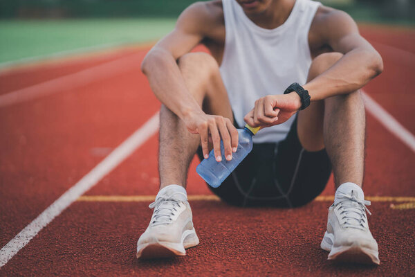 Athletes runner sport man resting holding bottle water tired and thirsty  practicing on a running track at a stadium. Running workout drinking water. Sport man run concept.