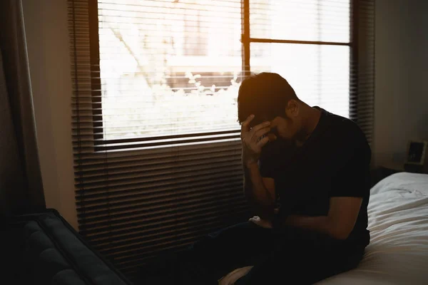 Sad asian man suffering depression insomnia awake and sit alone on the bed in bedroom. Silhouette depressed man sadly sitting on the bed in the bedroom, depression concept