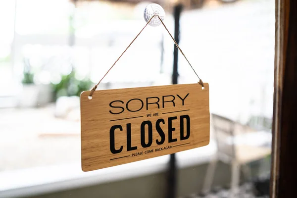 Close sign broad through the door glass. CLOSED sign board through the glass of store window. closed we are sorry text wooden board  door vintage shop sign close store.