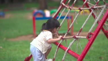 Cute asian girl smile play on school or kindergarten yard or playground. Healthy summer activity for children. Little asian girl climbing outdoors at playground. Child playing on outdoor playground.
