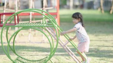 Cute asian girl smile play on school or kindergarten yard or playground. Healthy summer activity for children. Little asian girl climbing outdoors at playground. Child playing on outdoor playground.