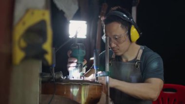 Gitarcı adam laboratuarda akustik gitar yapmak için kulaklık takıyor. Asyalı gitarcı el yapımı gitaristler için yüksek kaliteli gitarlar yapıyor. İyi marangoz ve geleneksel gitar çalıyor.