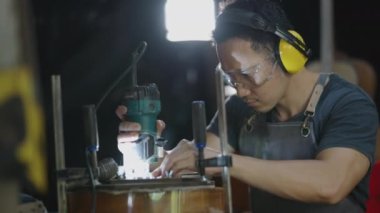 Gitarcı adam laboratuarda akustik gitar yapmak için kulaklık takıyor. Asyalı gitarcı el yapımı gitaristler için yüksek kaliteli gitarlar yapıyor. İyi marangoz ve geleneksel gitar çalıyor.