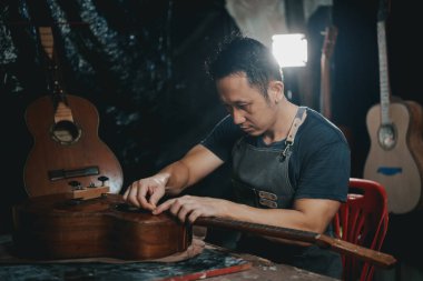 Gitar yapımcıları Asyalı adam laboratuarda akustik gitar yapıyor. Asyalı gitarcı, müzisyenler için el yapımı gitar dükkanı inşa ediyor. İnce ahşap işçiliği, gelenek, antik el sanatları.