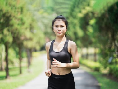 Asyalı kadın sporcu, formalı, siyah spor giysiler giyiyor ve koşarken ya da bahçede koşarken gülümsüyor, daha çok ağaç ve temiz hava alıyor, parkta egzersiz yapıyor. Spor sağlıklı çalışma konsepti.