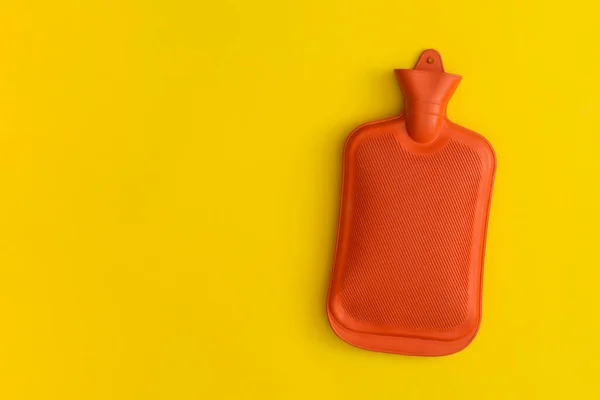 Hot water bottle on a yellow background. Top view with copy space. Flat lay.