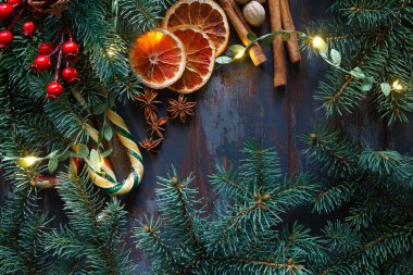 Köknar dalları, kırmızı böğürtlenler, kuru portakallar, baston şekerler, koyu mavi ahşap arka planda ışıklar ve eksiler olan Noel çerçevesi. Noel duvar kağıdı veya arkaplanı.