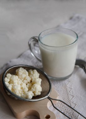 Süt kefir taneleri süzgeçte ve beyaz masada bir fincan kefir..