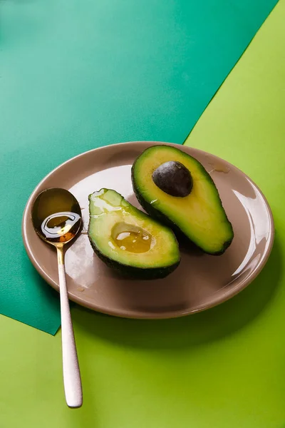 Zwei Scheiben Avocado auf rosa Teller mit einem Löffel auf grünem abstrakten geometrischen Hintergrund, Kopierraum — Stockfoto