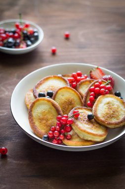 Böğürtlenli pankekler, kahverengi ahşap arka plan dikey fotoğraf üzerinde beyaz bir tabakta siyah ve kırmızı üzümlü üzümler.