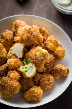 Kahverengi arka plan dikey fotoğrafında beyaz bir tabakta otlu ve soslu gevrek ekmekli karnabahar.