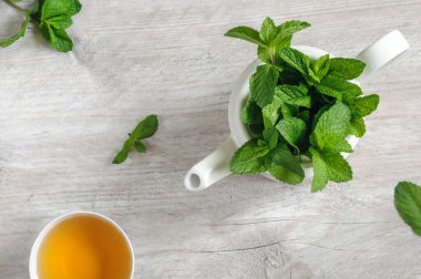 Taze nane yaprağı, çaydanlık ve gri ahşap zemin üzerinde bir fincan nane çayı. Üst görünüm, gün ışığında seçici odaklanma