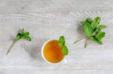Gri ahşap arka planda, nane yapraklı beyaz bir fincanda taze nane çayı. Üst görünüm, kopyalama alanı ile seçici odak