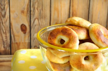 Yuvarlak kurabiyeler, ortasında bir delik olan cam bir kase ile ahşap bir duvara karşı. Seçici odaklanma. Boşluğu kopyala