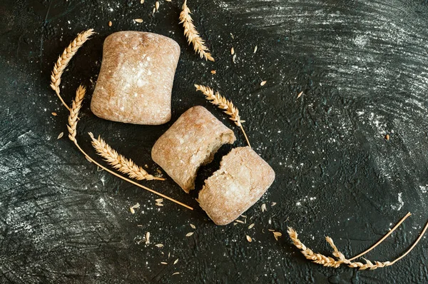 小麦粉と小麦の耳を持つ黒の背景に2つの部分に分割1パンの形でイタリアのパンのクローズアップ トップビュー 選択的な焦点と自然光とフラットレイアウト — ストック写真