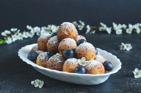 Ev yapımı süzme peynirli çörekler pudra şekeri ve kiraz çiçekli, gri bir arka planda böğürtlenli. Gün ışığı, tonlu resim, seçici odak