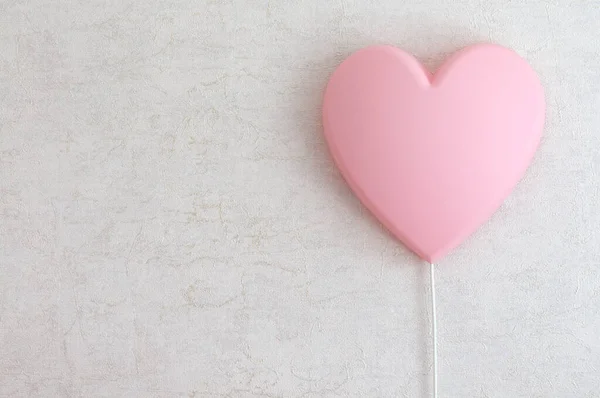 A pink lamp in the shape of a heart on a light wall in the room. Selective focus with copy space, natural light