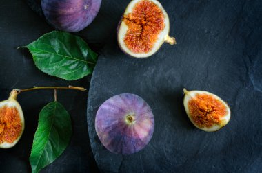 Siyah arka planda taze incir yapraklar ve meyve parçaları. Seçici odak, üst görünüm