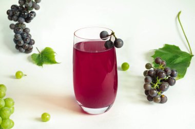 Bir bardak taze sıkılmış üzüm suyu ve açık gri arka planda bir demet üzüm. Doğal ışık, seçici odaklanma