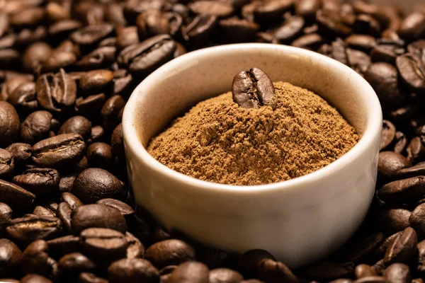 Kahve çekirdeğinin arka planında beyaz bir seramik kasede öğütülmüş tarçın.