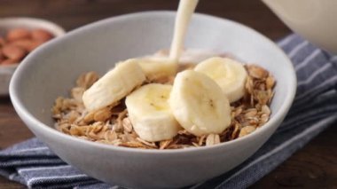 Muz taneciklerinin içine soya sütü dökülüyor, ağır çekimde. Sağlıklı kahvaltı.