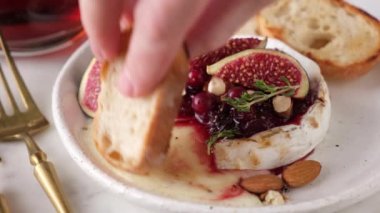 İncirli, fındıklı ve ballı peynirli camembert peyniri. Kızarmış baget dilimlenmiş kadın eldiveni erimiş peynirin içine yakın çekim görüntüsü. Gurme yemekleri.