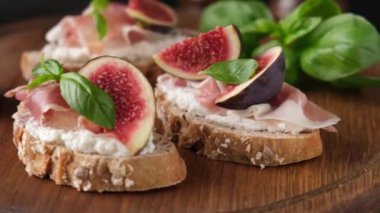 Tahta servis tahtasında fesleğen ve balla süslenmiş incirli prosciutto bruschetta. Yakın çekim.