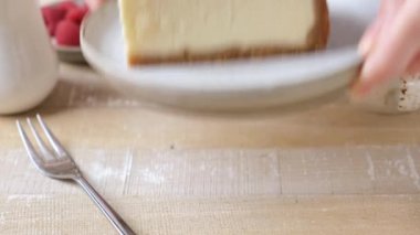 Tabakta bir dilim cheesecake servis ediyorum. Kadın elleri, üzerinde ahşap bir masanın üstünde taze ahududu bulunan bir dilim New York peynirli kekle tabağı koyuyor.