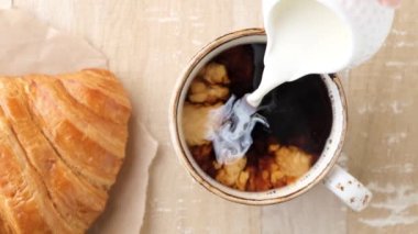 Yavaş çekimde sütlü sütü sade kahveye dök. Üst Manzara. Kruvasanla kahve.