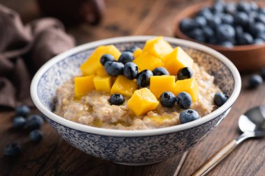 Mangolu yulaf ezmesi kasesi ve ahşap masa arkasında yabanmersini, yakın çekim manzarası. Sağlıklı vejetaryen kahvaltısı