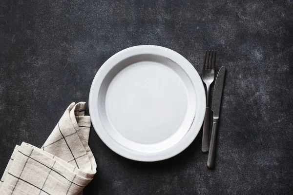 Empty plate, cutlery and linen table textile on black concrete table background. Top view copy space. Kitchen table setting
