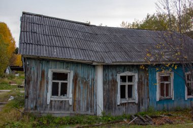 Sonbahar çalılıklarında terk edilmiş bir köy evi. Sonbahar ağaçları ve küçük ahşap bir evin kalıntıları..