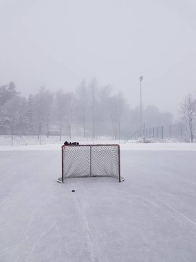 Ice hockey goal, puck and gloves on outdoor ice rink with misty background.